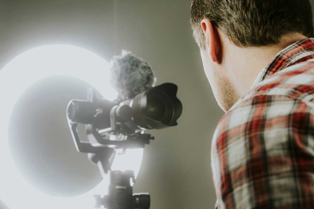 A man uses a ring light to light up his face for a Camera recording.