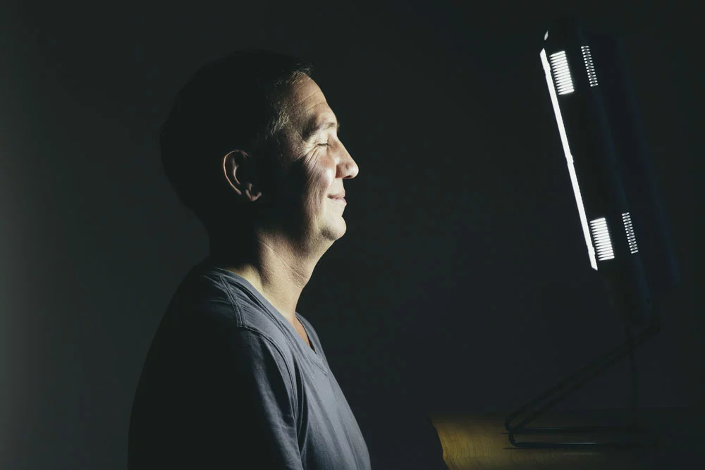 A man sitting in front of a full spectrum light therapy box, which mimics sunlight