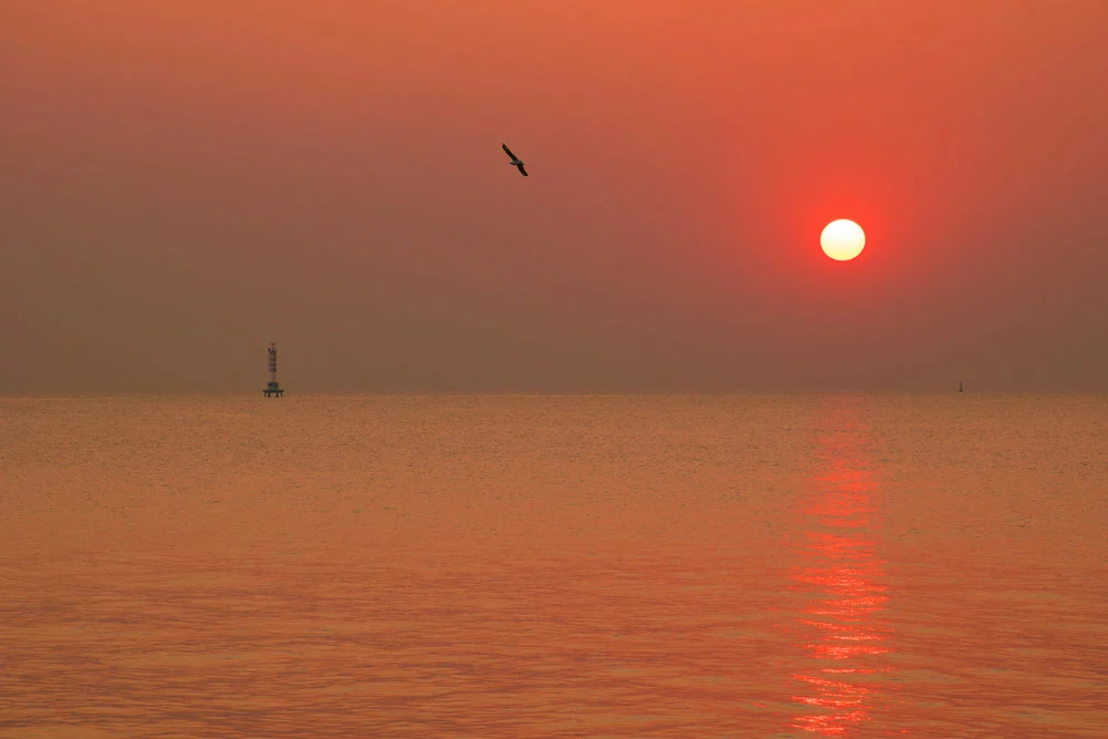 A sunset at sea signifies the beginning of dusk.