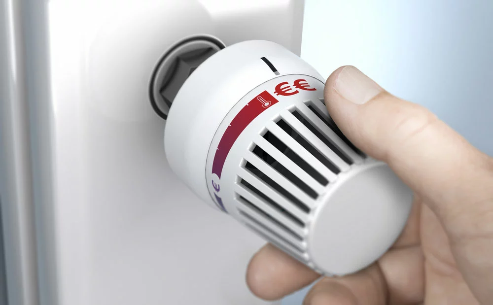 Hand-turning a thermostat knob to increase savings by decreasing energy consumption