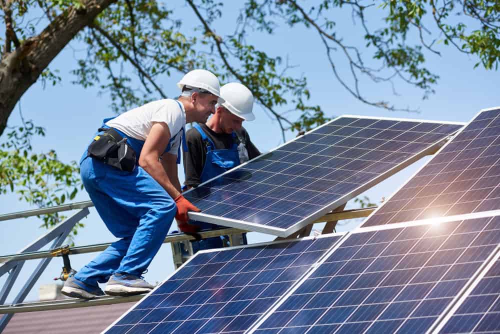 Two young technicians installing heavy solar photo voltaic panel