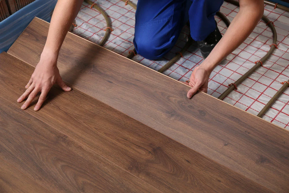 Worker installing laminate flooring atop the radiant heating system.