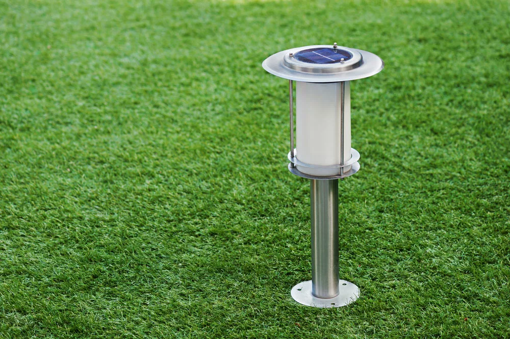 Solar vs. Wired Landscape Lighting: Solar-powered lamp on green grass background.