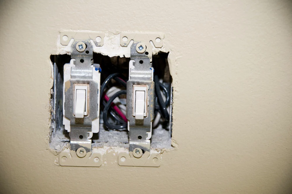 Light switches are installed on a switch box on a wall without the cover plate.